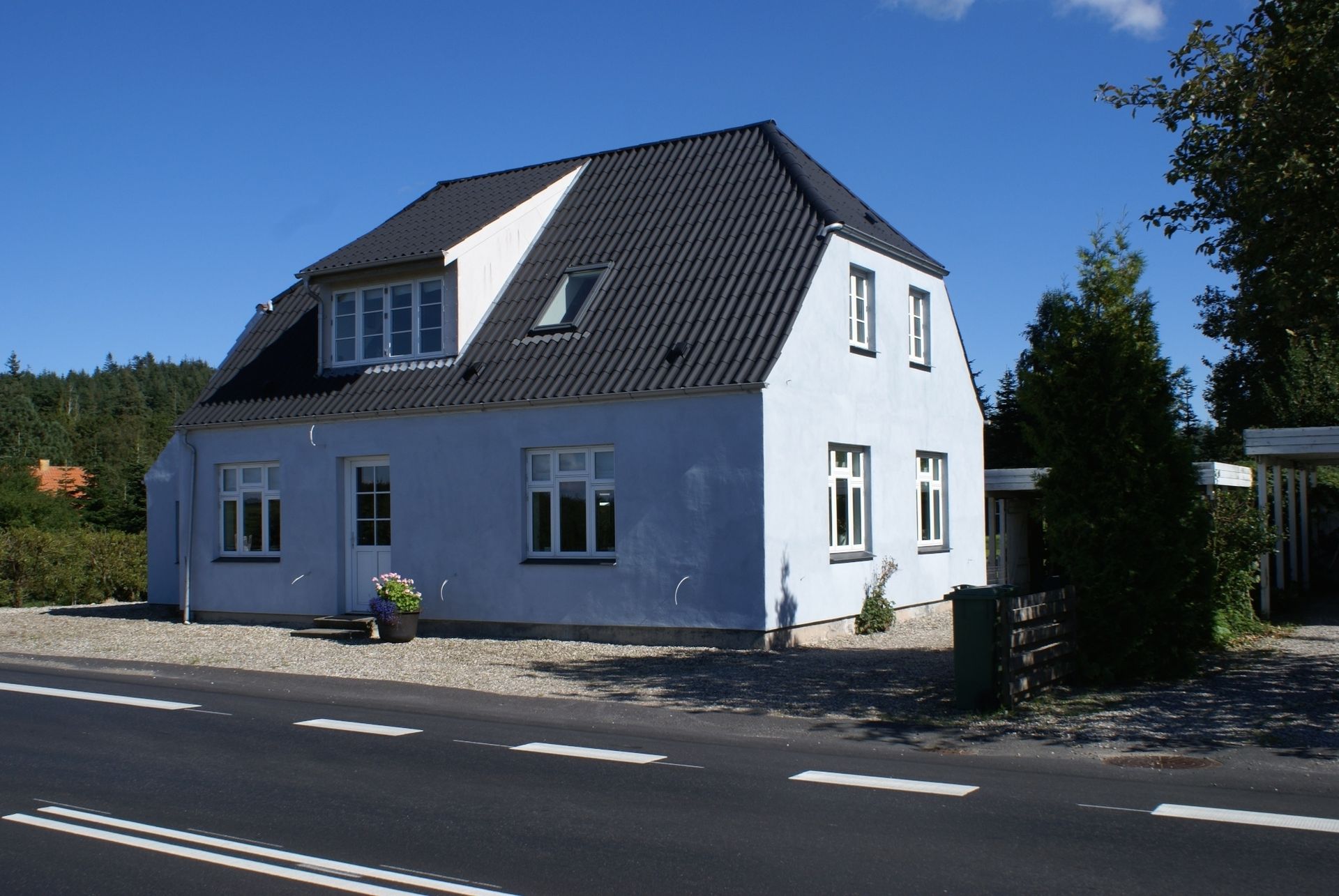 Blegblåt hus med mørkegråt tag, beliggenhed ved vejkanten.