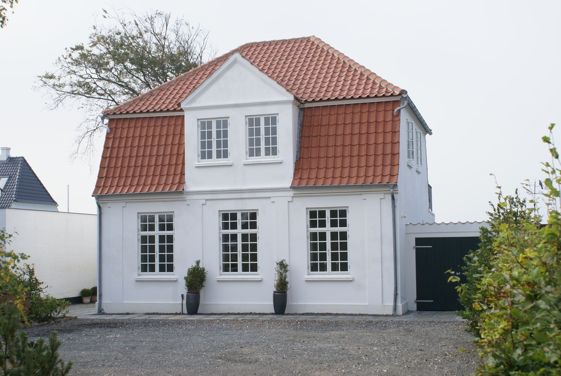 Hvidt toetagers hus med rødt tegltag, flere vinduer og en mørkegrøn garageport.