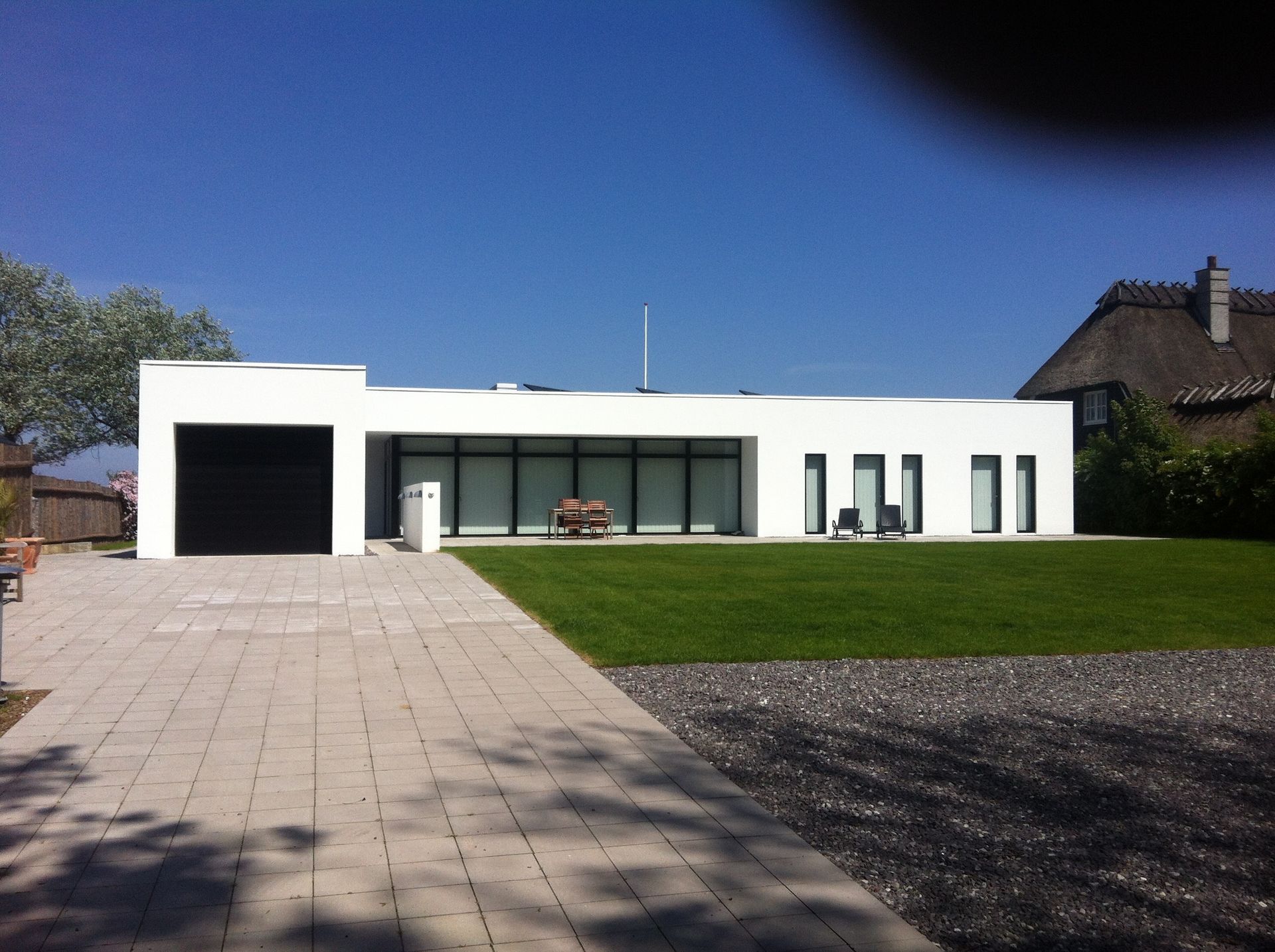 Hvidt moderne hus med sort garageport og store vinduer, på en grøn græsplæne med en klar blå himmel.