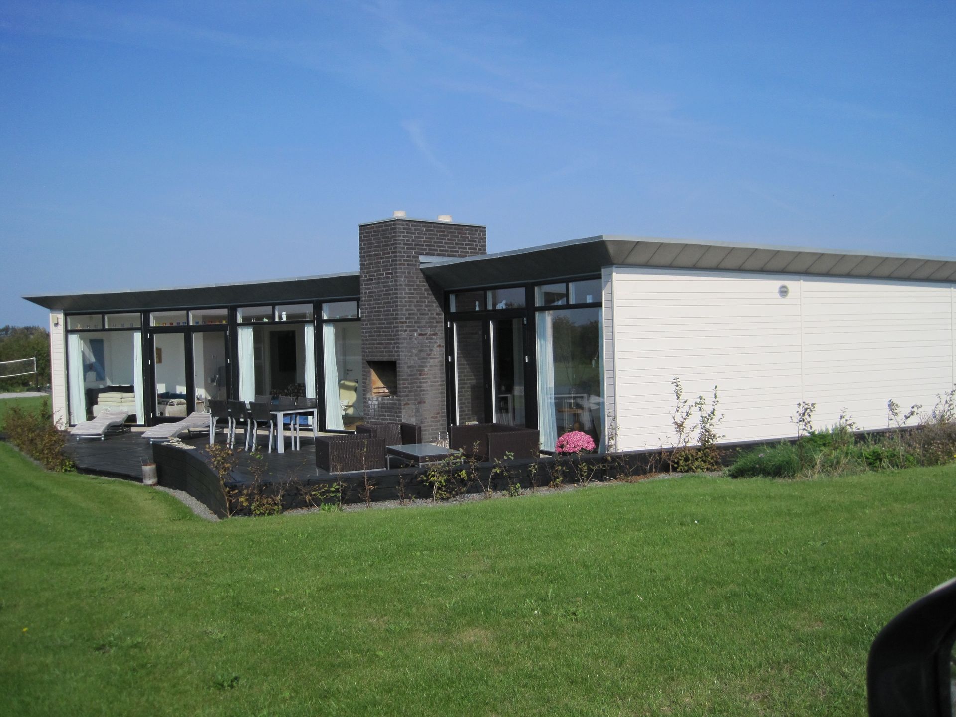Moderne hvidt hus med mørke lister og en sort murstensskorsten, beliggende på grønt græs under en blå himmel.