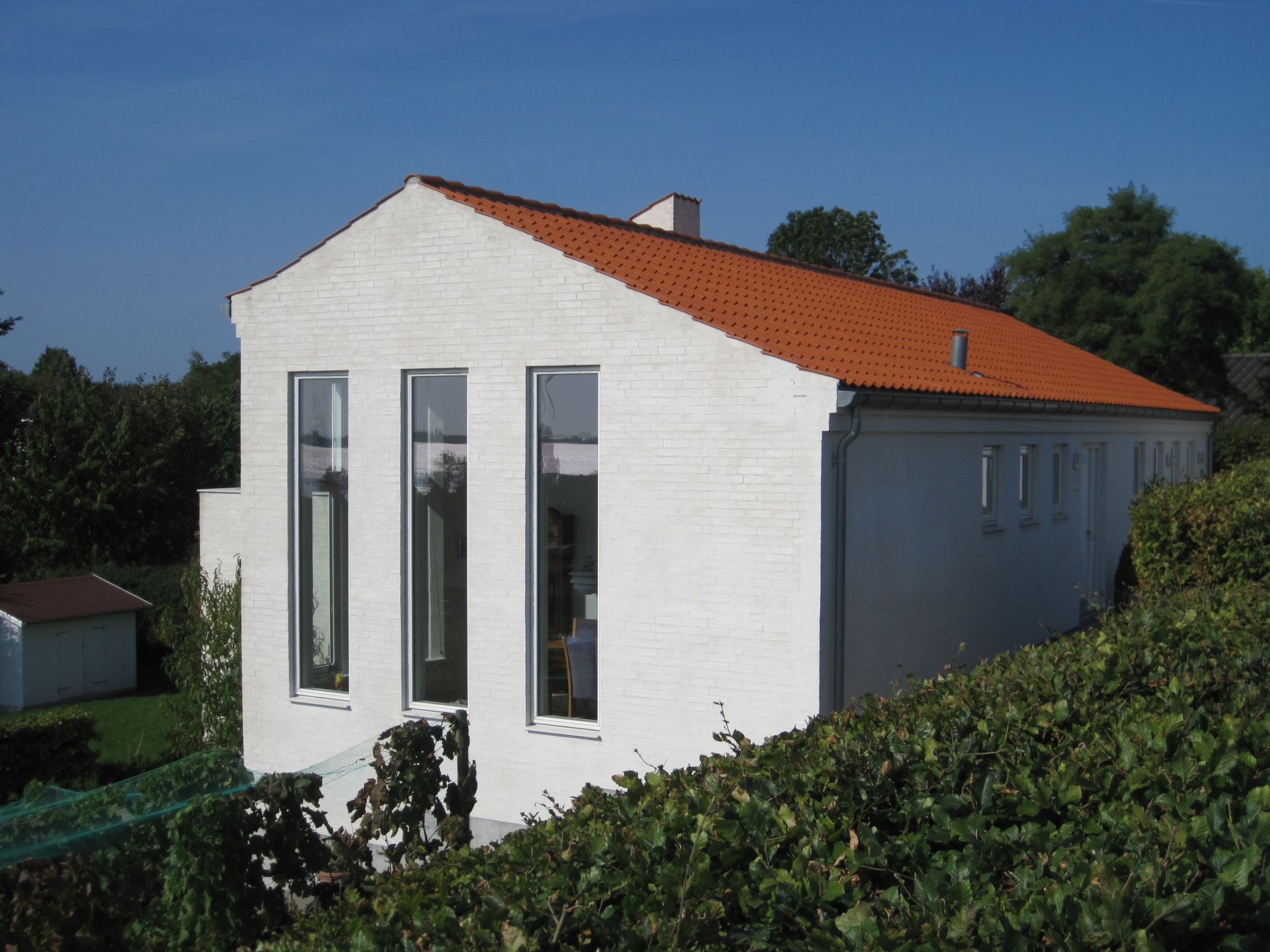 Hvid bygning med rødt tegltag, høje vinduer og et grønt landskab.