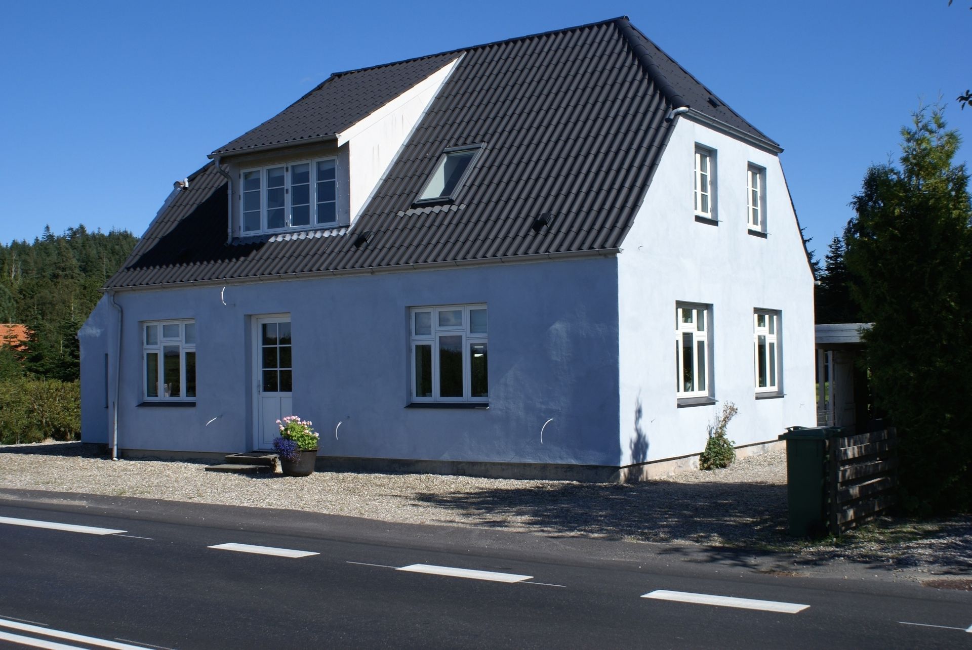 Blåt hus med sort tag, flere vinduer og en kvist mod en blå himmel.