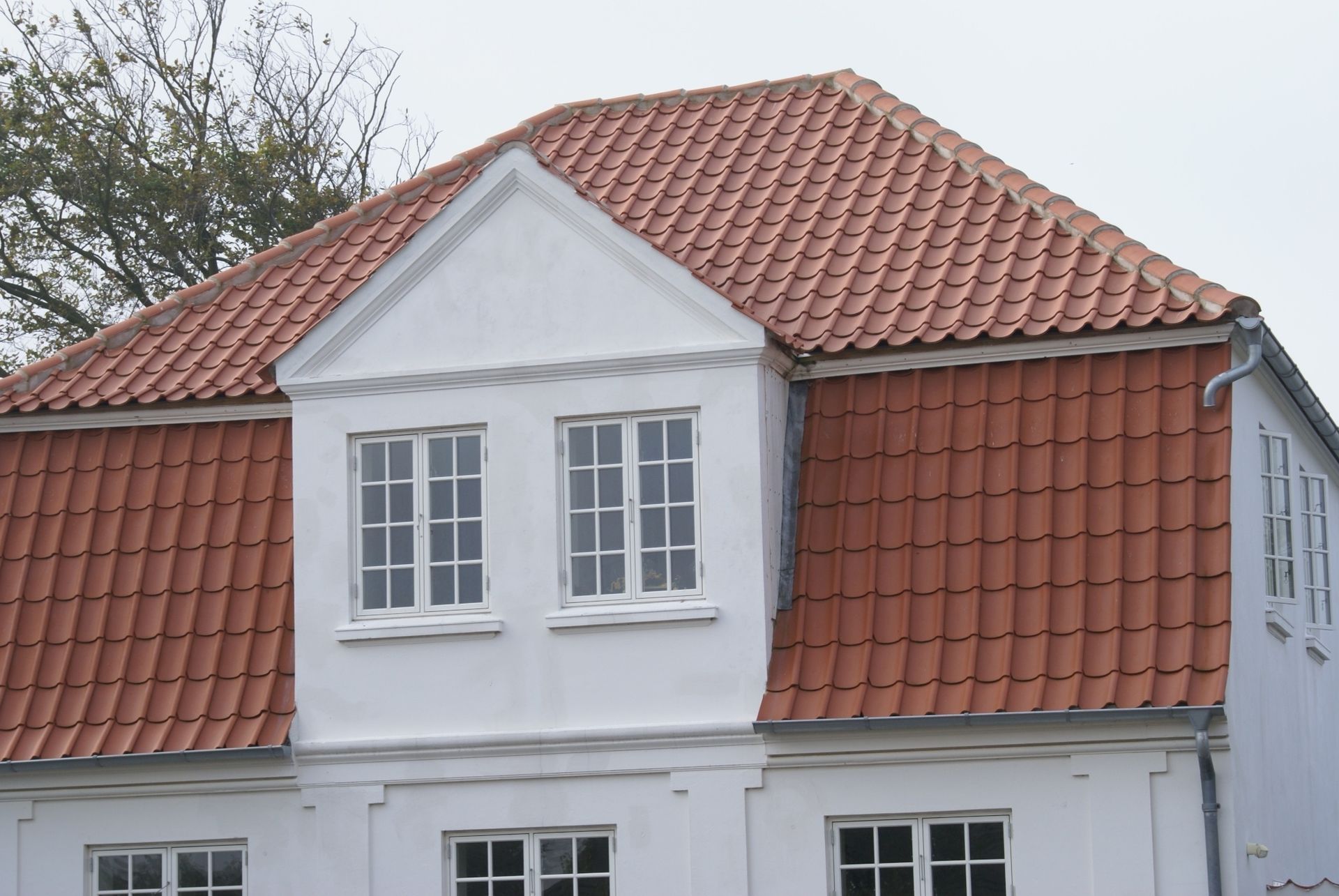 Hvid bygning med rødt tegltag, to vinduer i midten og en siderende.