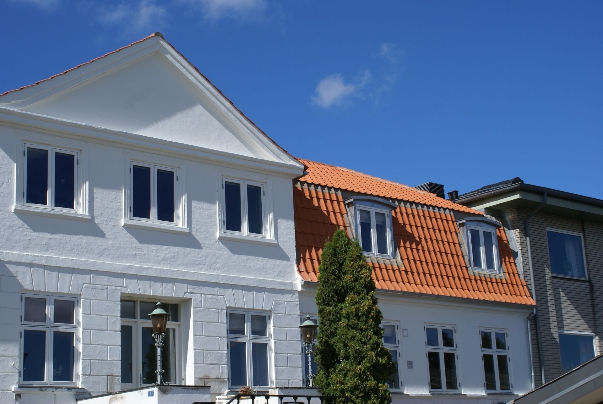 Hvid bygning med orange tegltag mod en blå himmel.