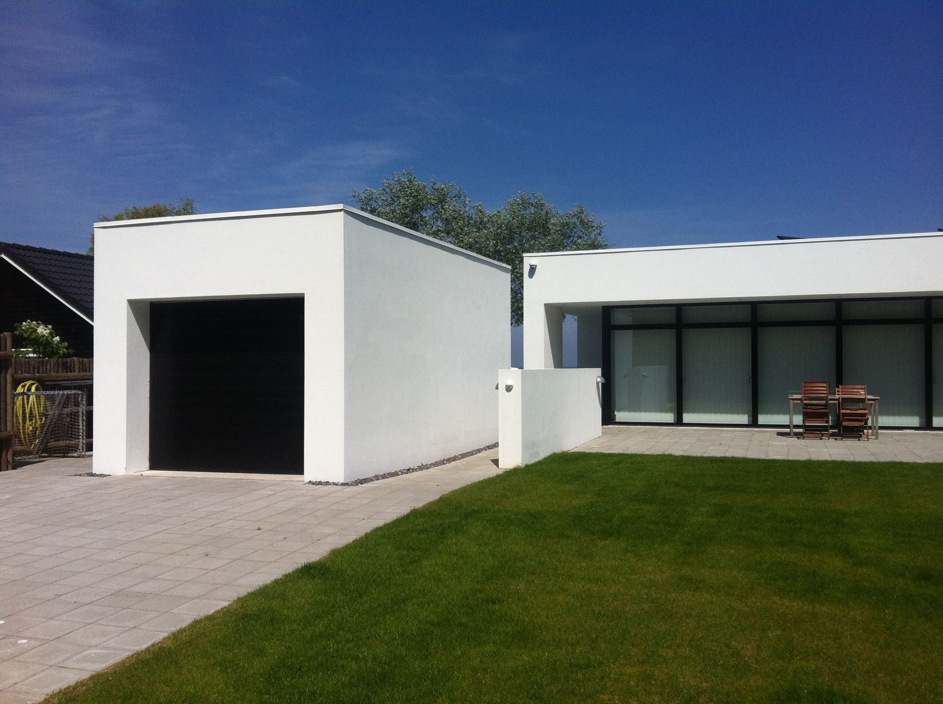Hvid garage og moderne hus med glasvinduer på en solskinsdag. Grøn græsplæne foran.