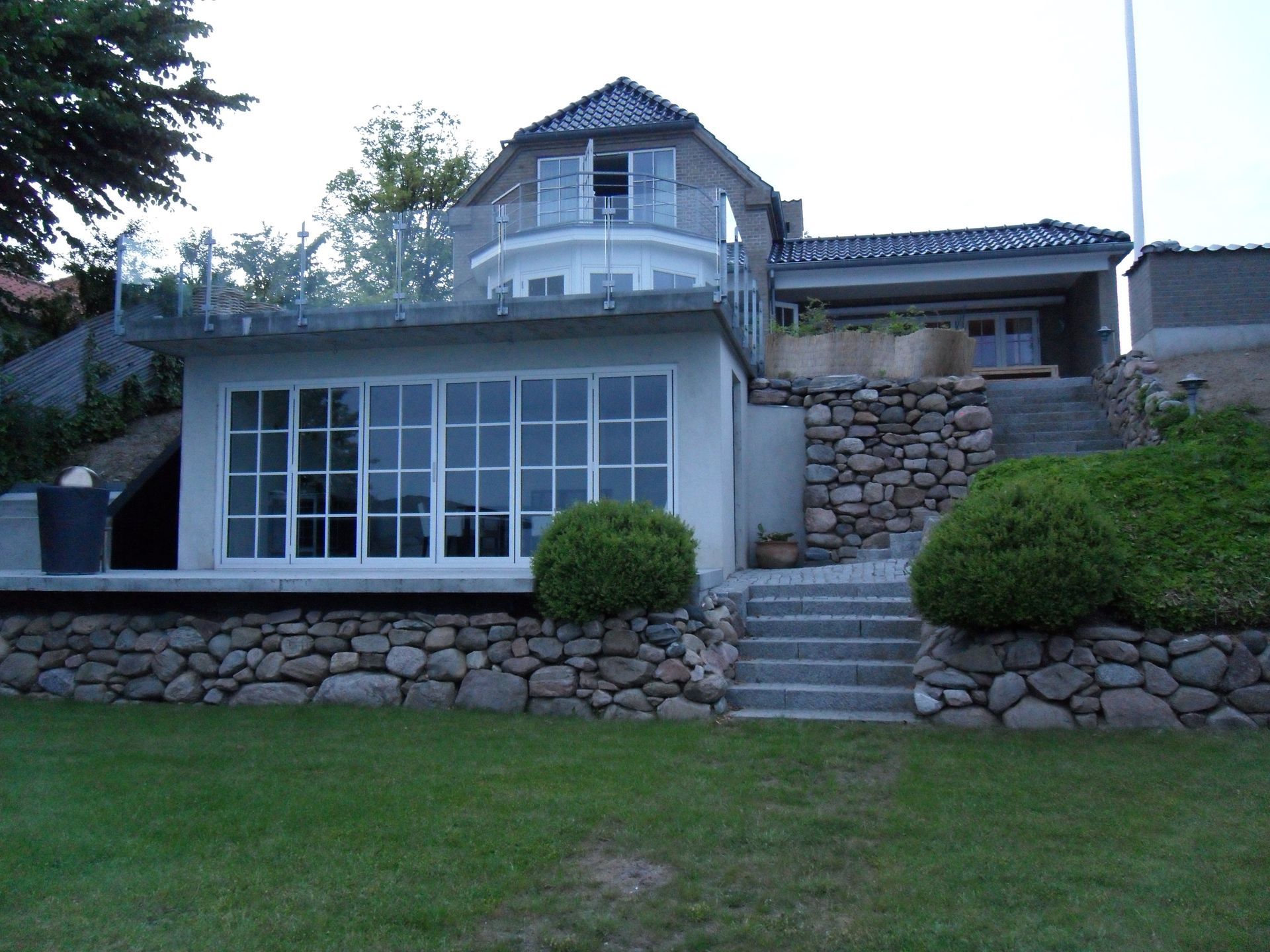 Kysthus med flere etager, stenstøttemure og store vinduer.