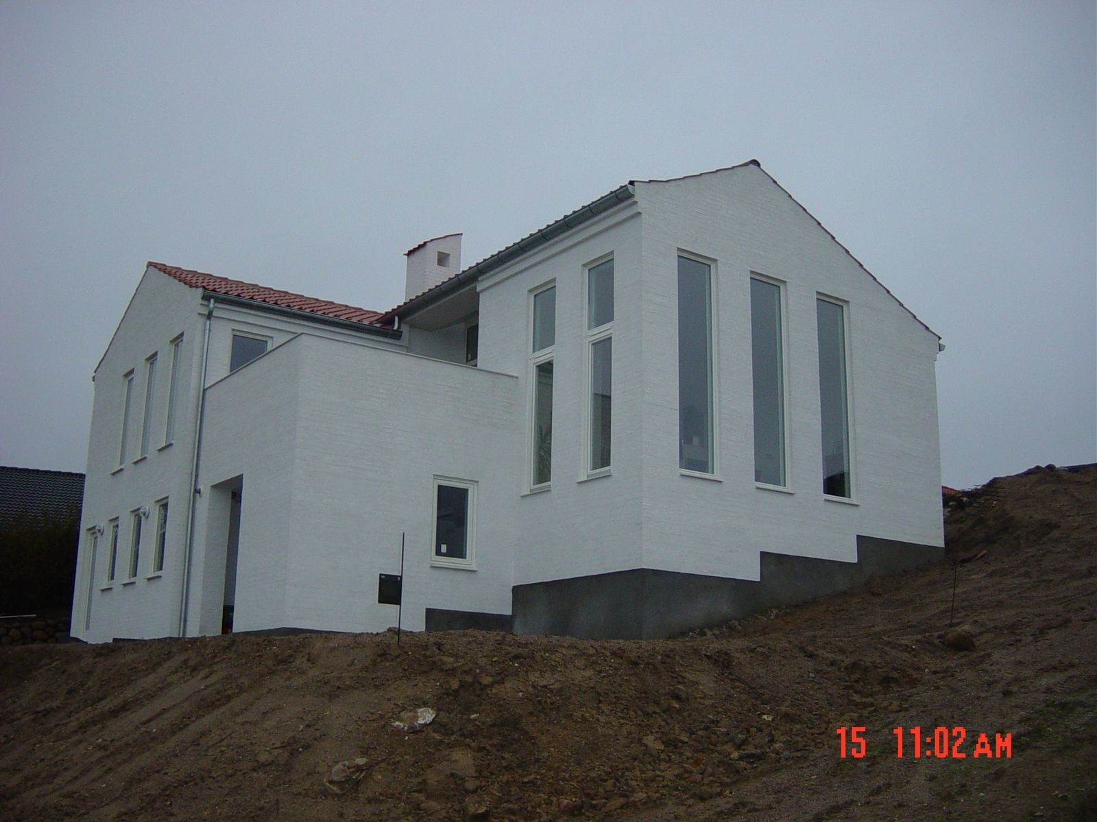 Hvidt hus med høje, smalle vinduer, på en jordhøj under en overskyet himmel.