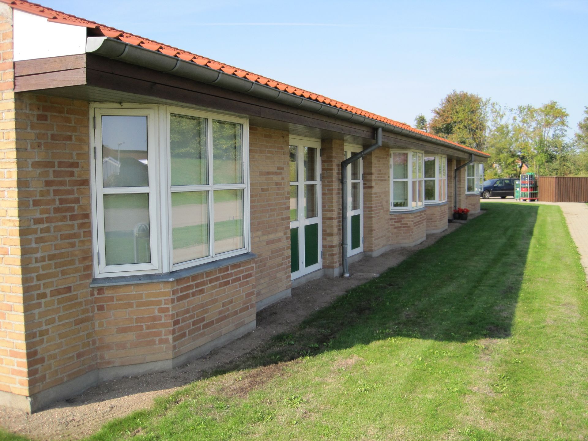 Murstensbygning med flere vinduer og en grøn græsplæne, solskinsdag.