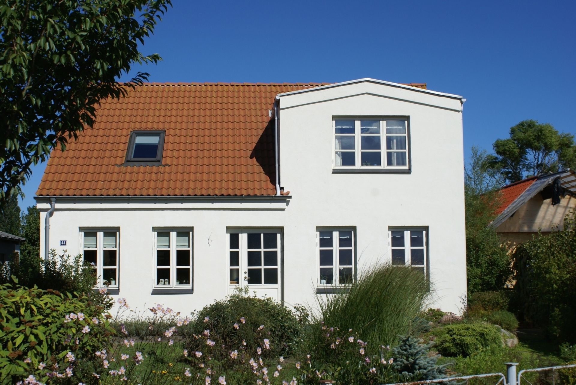 Hvidt hus med rødt tegltag, flere vinduer og en blå himmel i baggrunden.