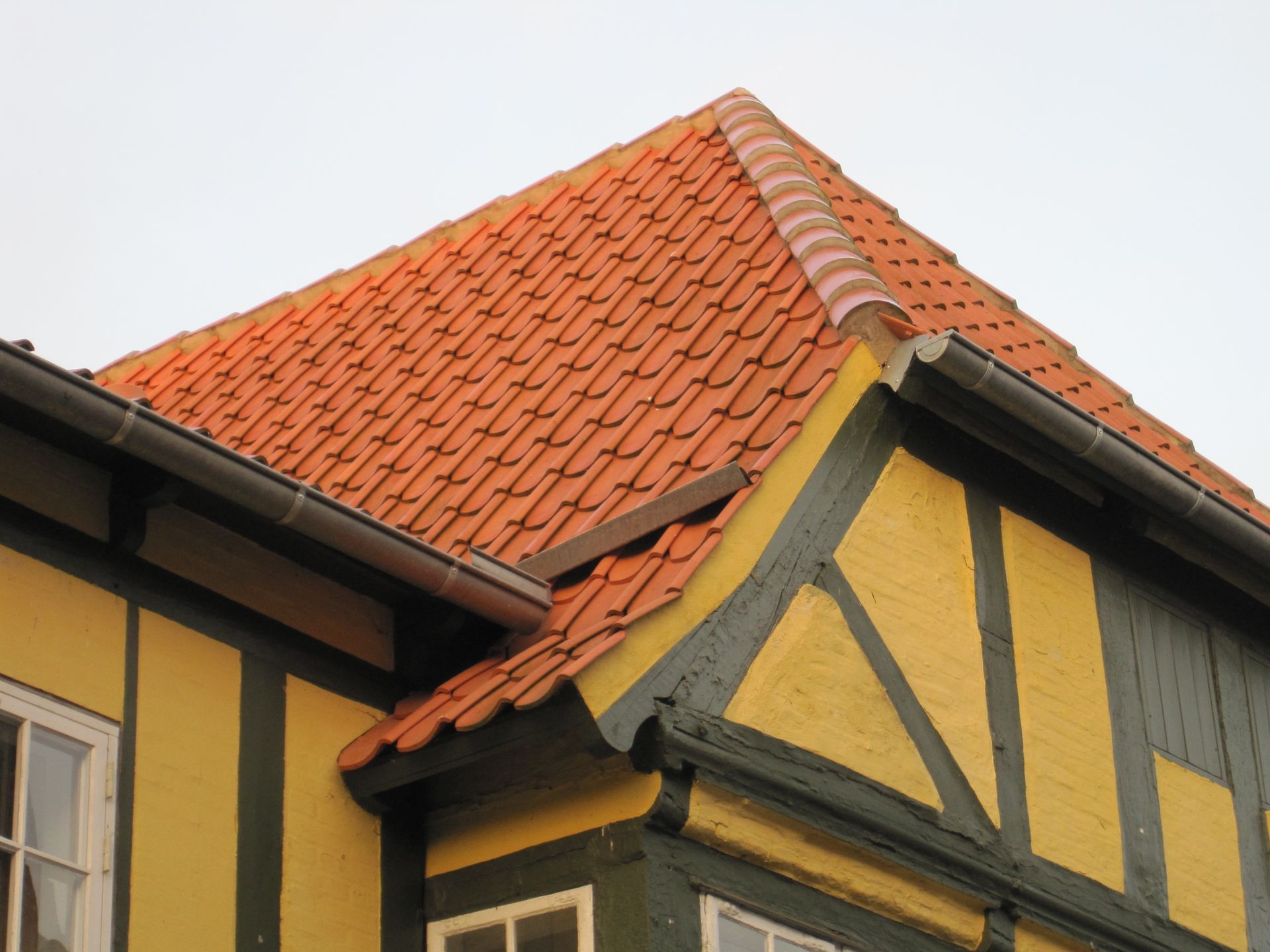 Gul bindingsværksbygning med orange tegltag, sorte lister og tagrende.