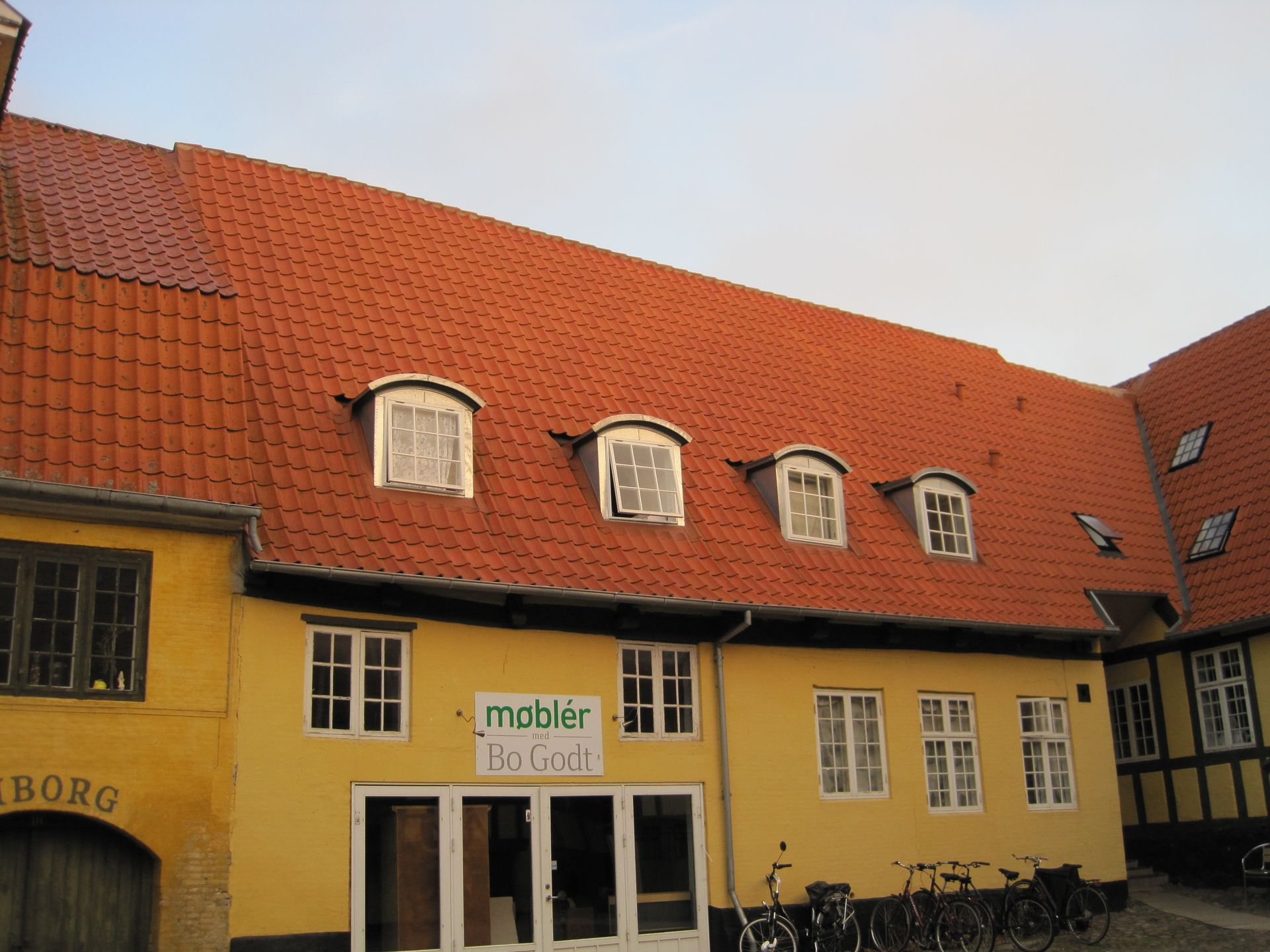 Gul bygning med rødt tegltag, kvistvinduer og et 