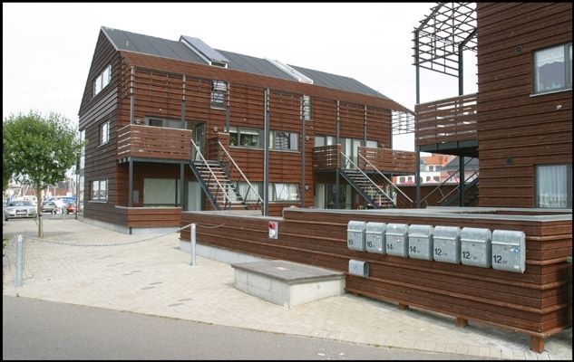 Brun træbygning i flere etager med udvendig trappe og postkasser.