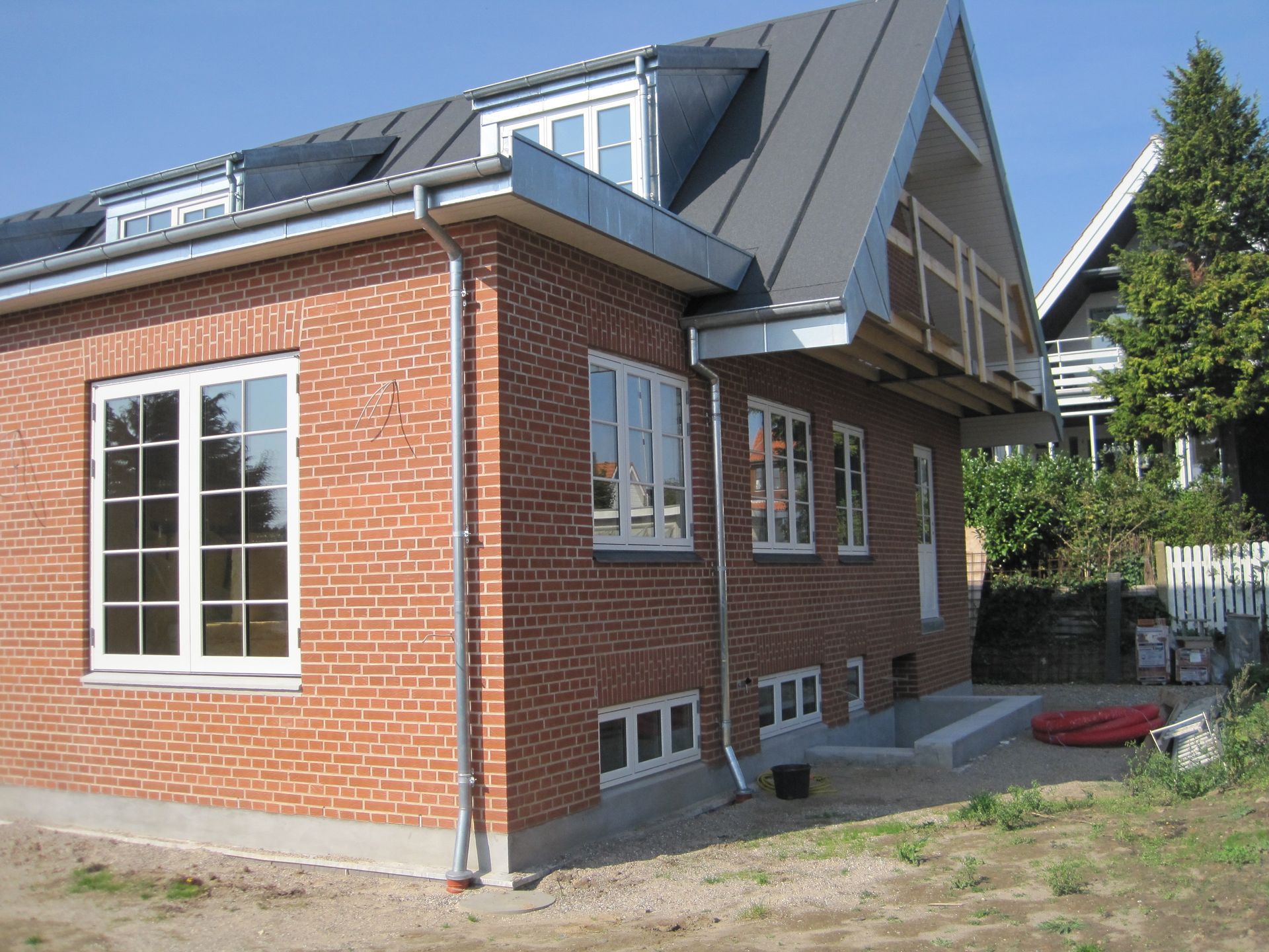 Rødt murstenshus med hvidindrammede vinduer, mørkegråt tag og metalrender.