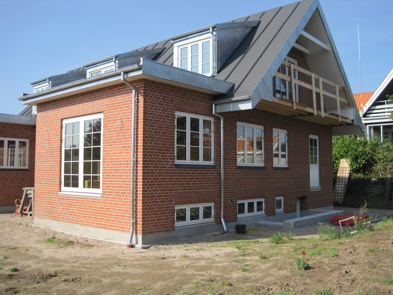 Murstensbygning med gråt tag, hvidindrammede vinduer og en lille balkon på en solskinsdag.