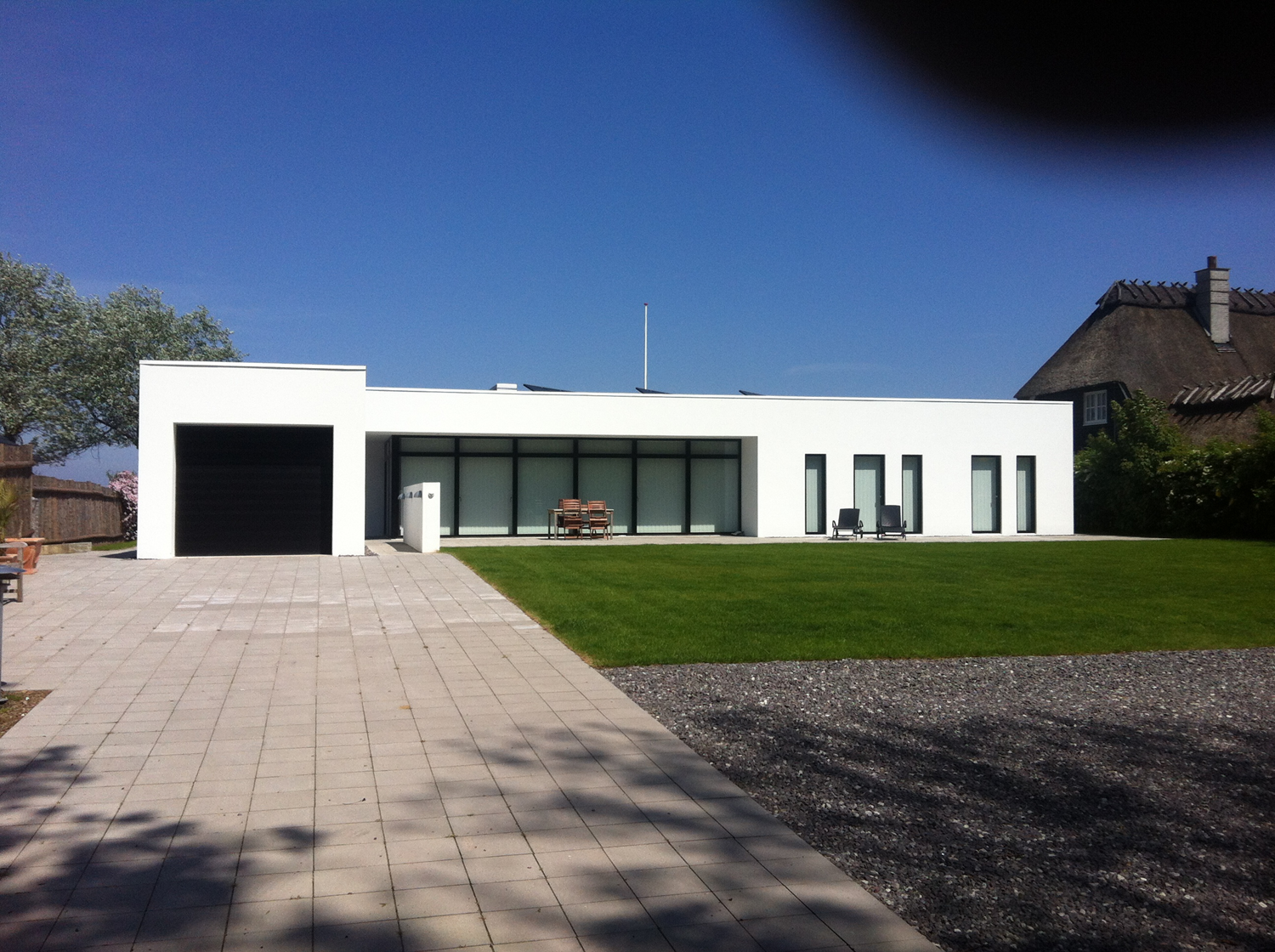 Moderne hvidt hus med sort garageport, glasvinduer og grøn græsplæne på en solskinsdag.