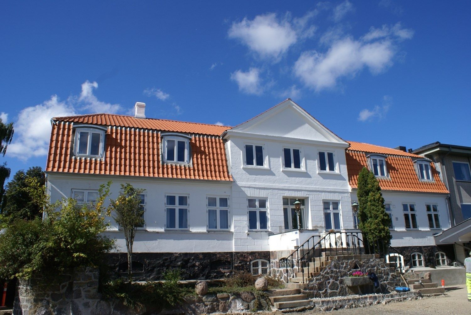 Hvid bygning med orange tegltag under en blå himmel med skyer.