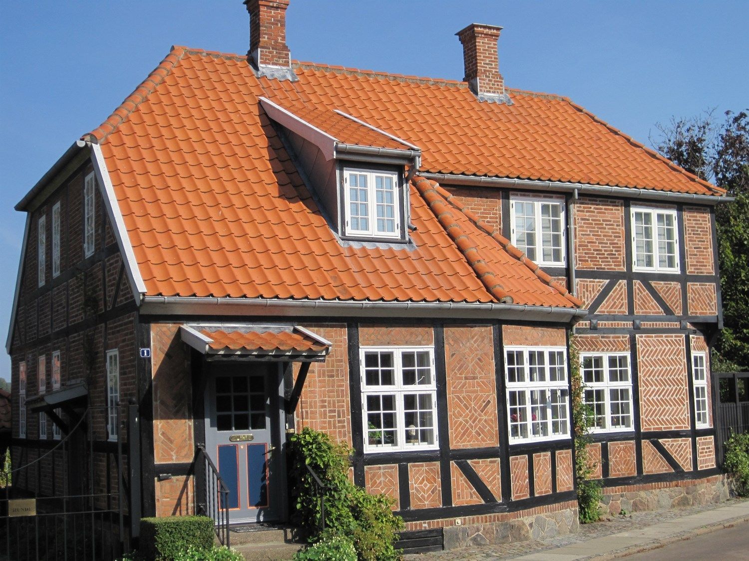 Murstenshus med orange tegltag og sort og hvid bindingsværkskonstruktion.