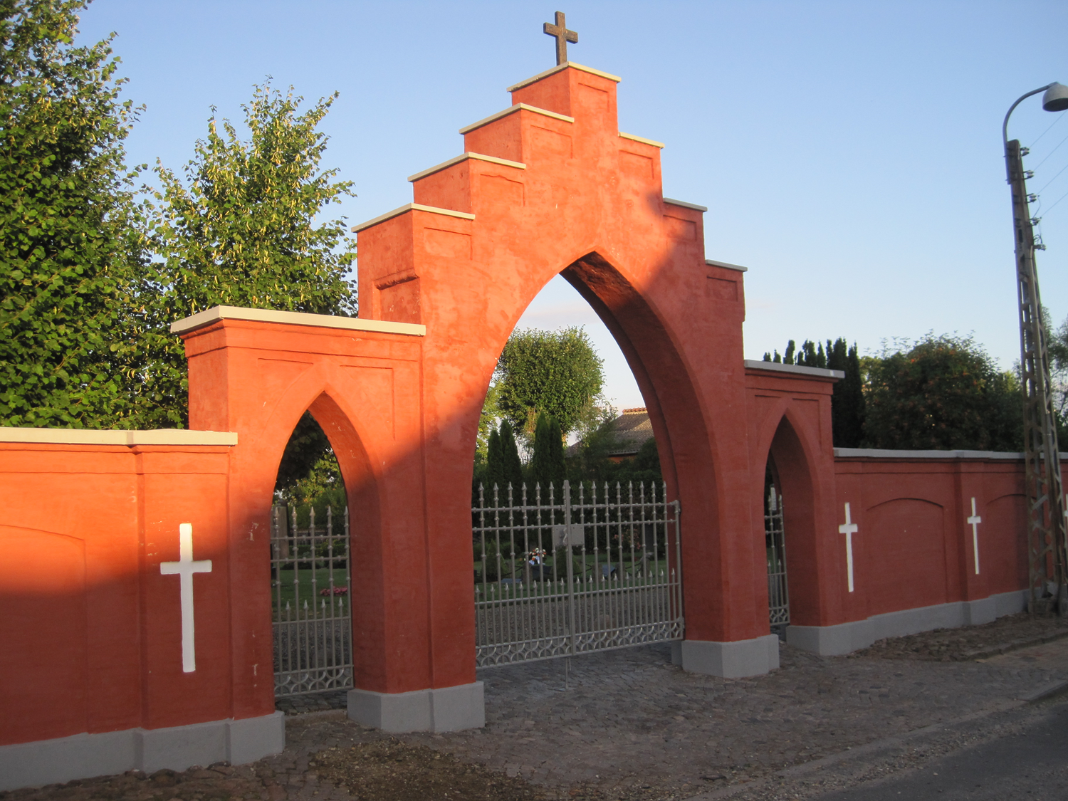 Rød buet kirkegårdsindgang med kors på toppen og hvide kors på væggen.