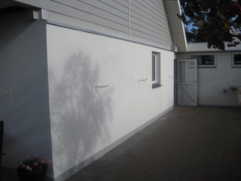 Hvid bygningsfacade med en dør, et vindue og en lille terrasse.