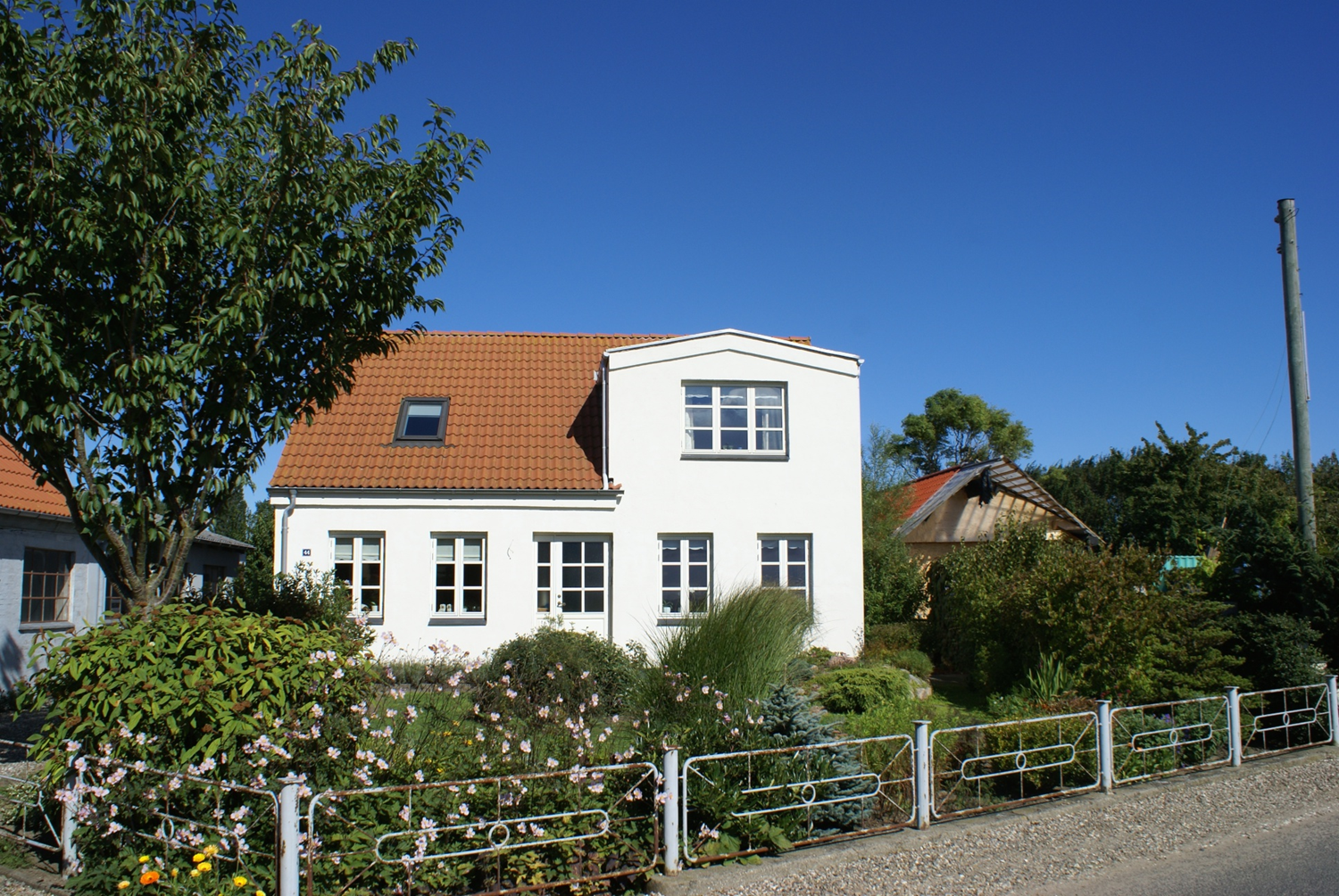 Hvidt hus med rødt tag og have, blå himmel.