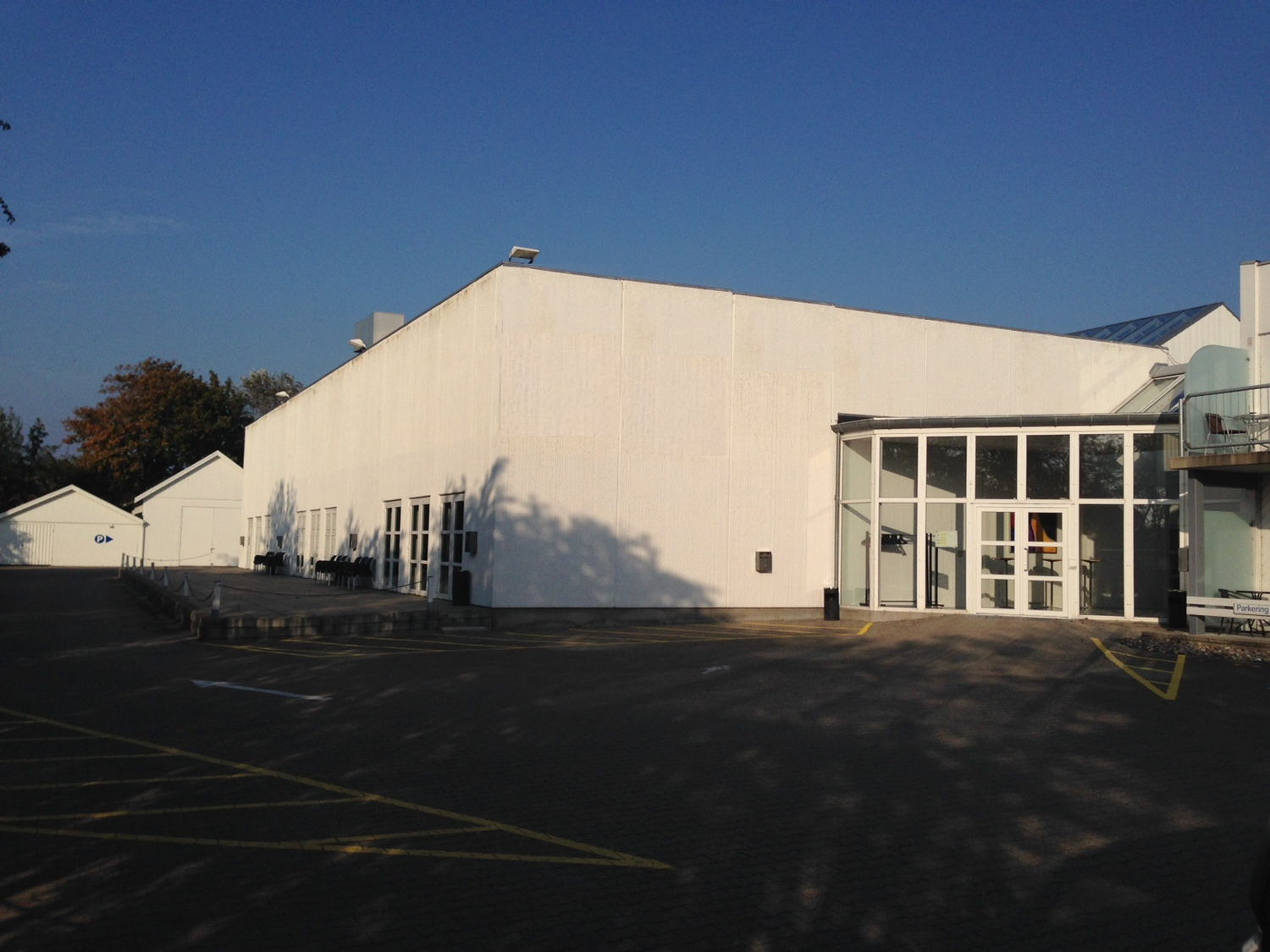 Hvid bygning med glasindgang, blå himmel.