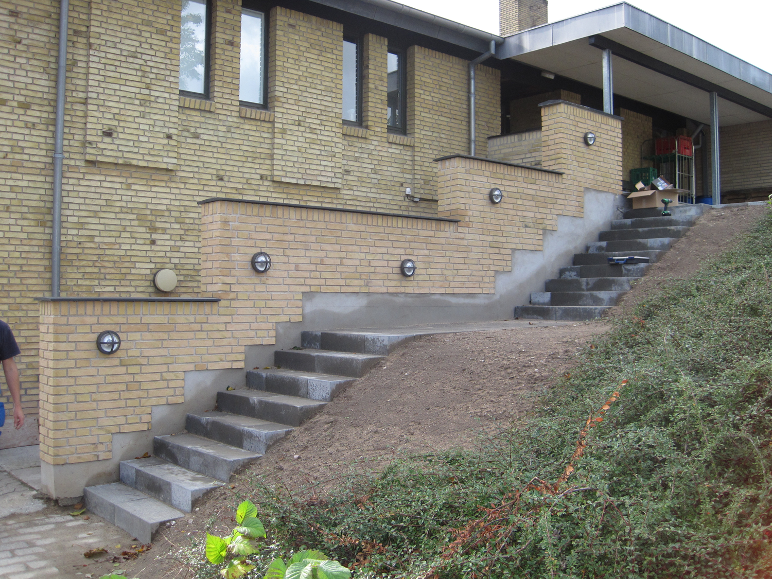 Murstensbygning med udendørs trappe og grusvej.