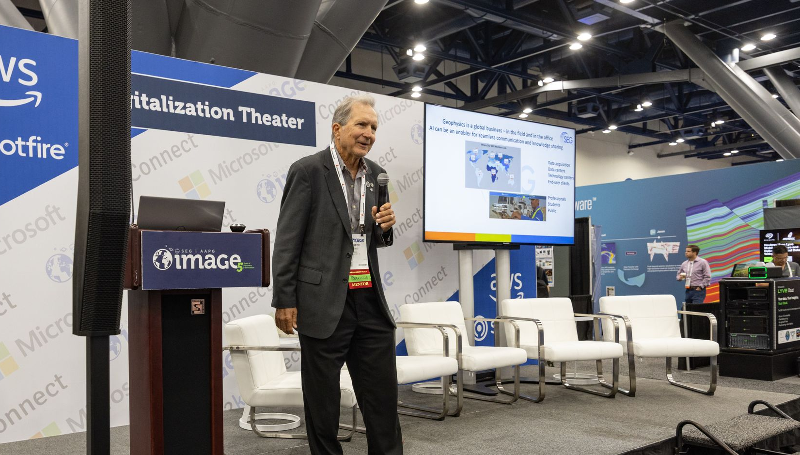 Man presenting at a conference, standing in front of a screen displaying diagrams.