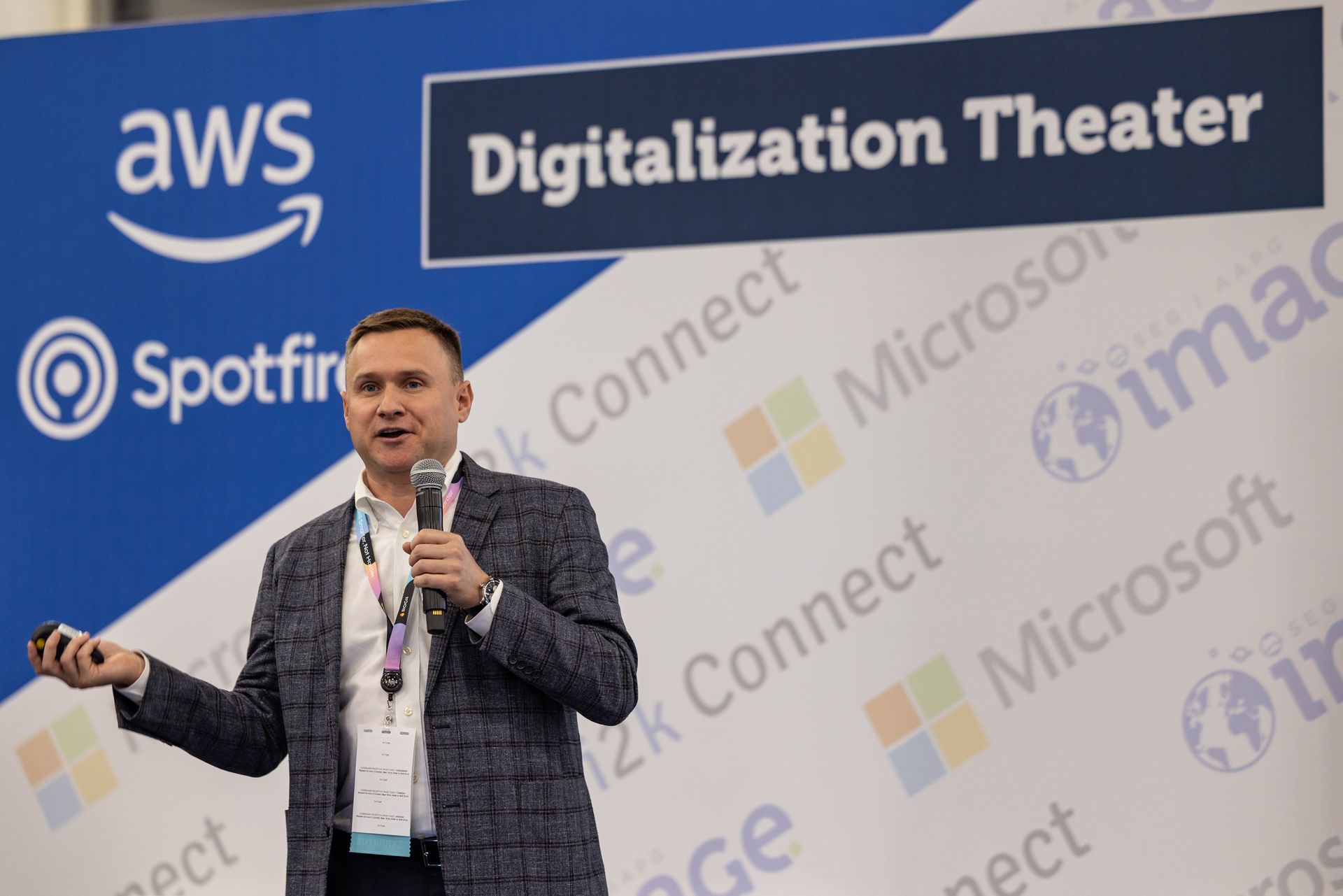 Man speaking at a conference. The backdrop has logos for AWS, Spotfire, and Microsoft.