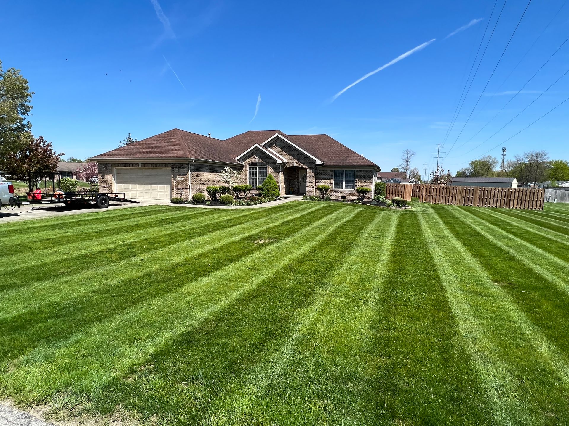 Lawn striped in alternating light and dark green, in front of a brick house on a sunny day.