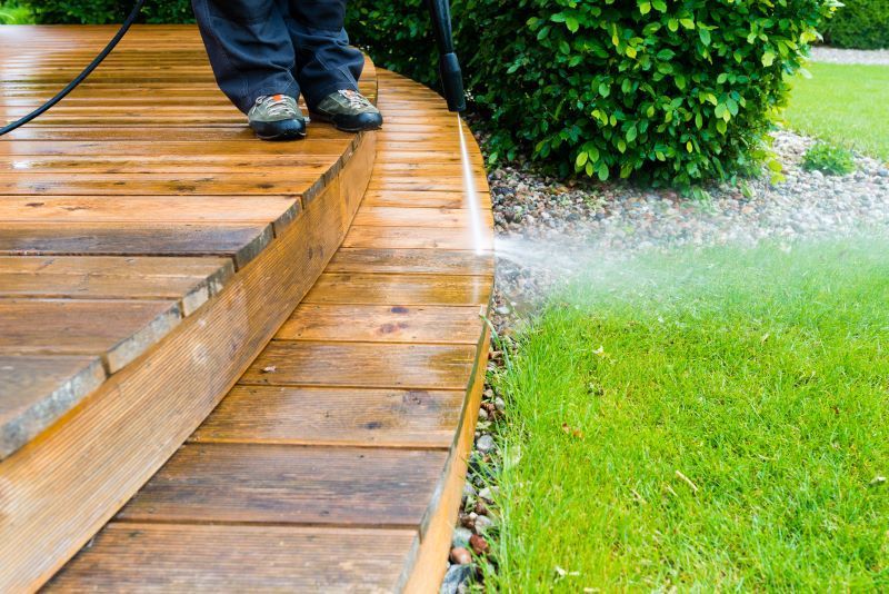 A person is cleaning a wooden deck with a high pressure washer.