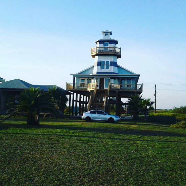 A white car is parked in front of a house that looks like a lighthouse