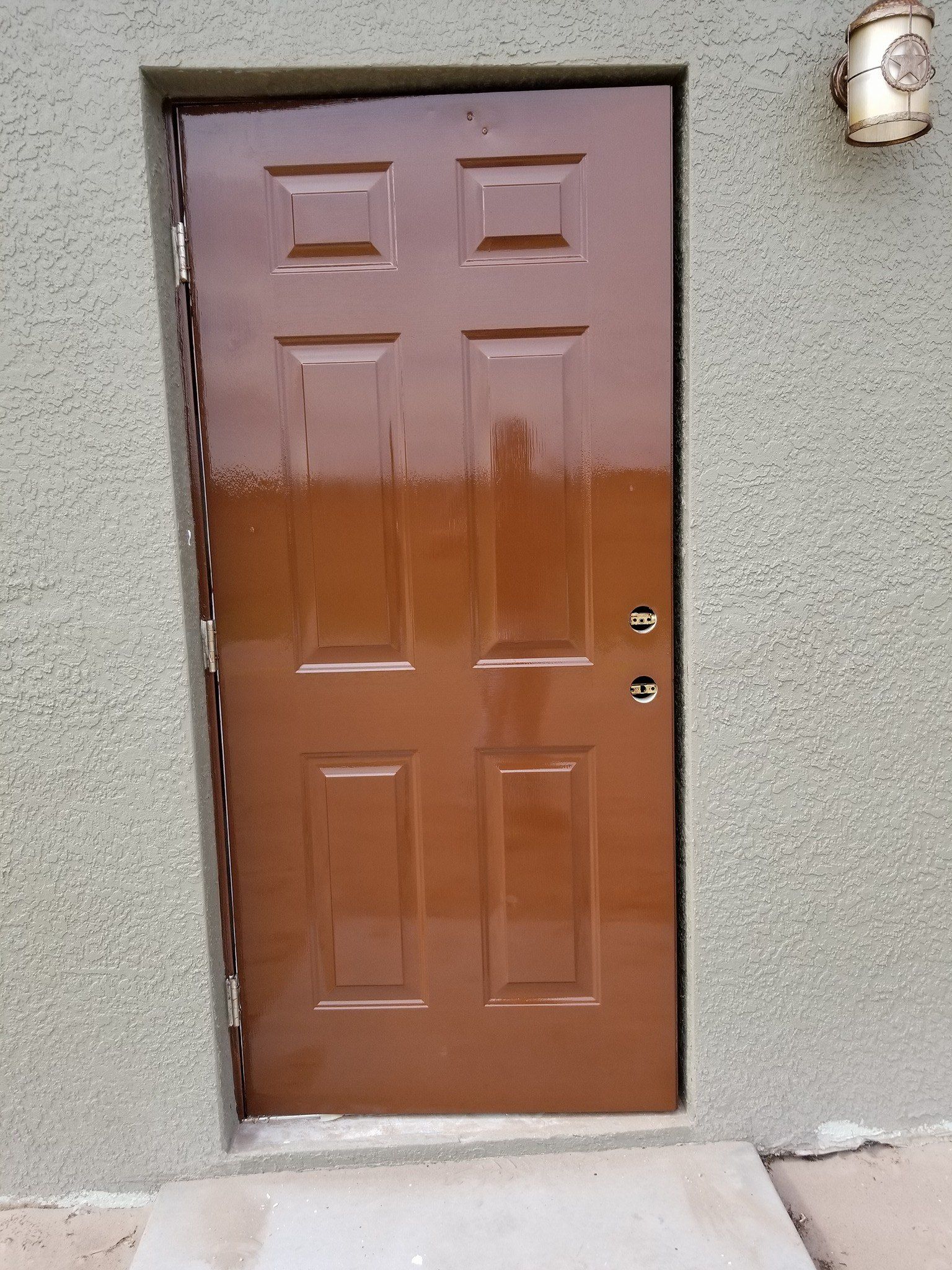 A brown door is on a gray wall next to a light.