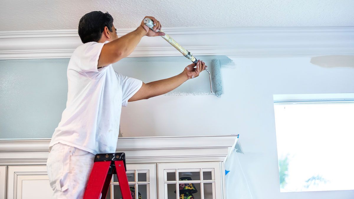 A man is standing on a ladder painting a wall.