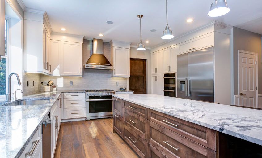 A kitchen with white cabinets , marble counter tops , stainless steel appliances and a large island.