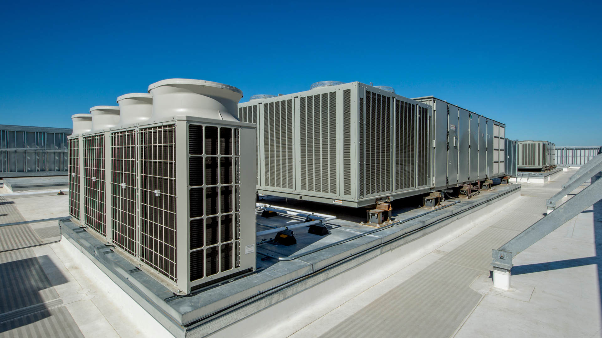 Large industrial HVAC units on a flat building rooftop under a clear blue sky.