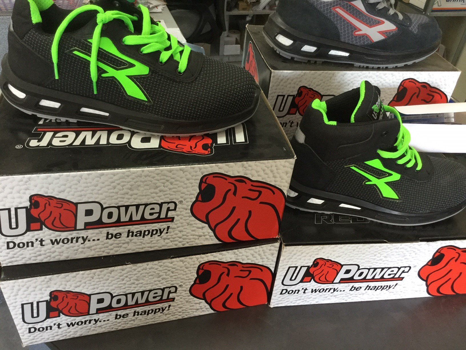 Scarpe da lavoro U-Power nere e verdi, confezionate in scatole. Lacci e dettagli verde neon. Le scatole presentano il logo di un bulldog.