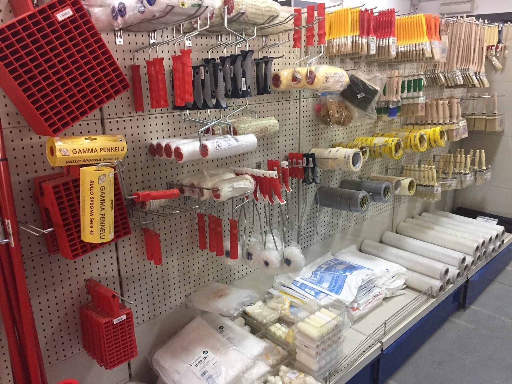 Forniture per la pittura: rulli, pennelli, vassoi e altri strumenti esposti sugli scaffali di un negozio.