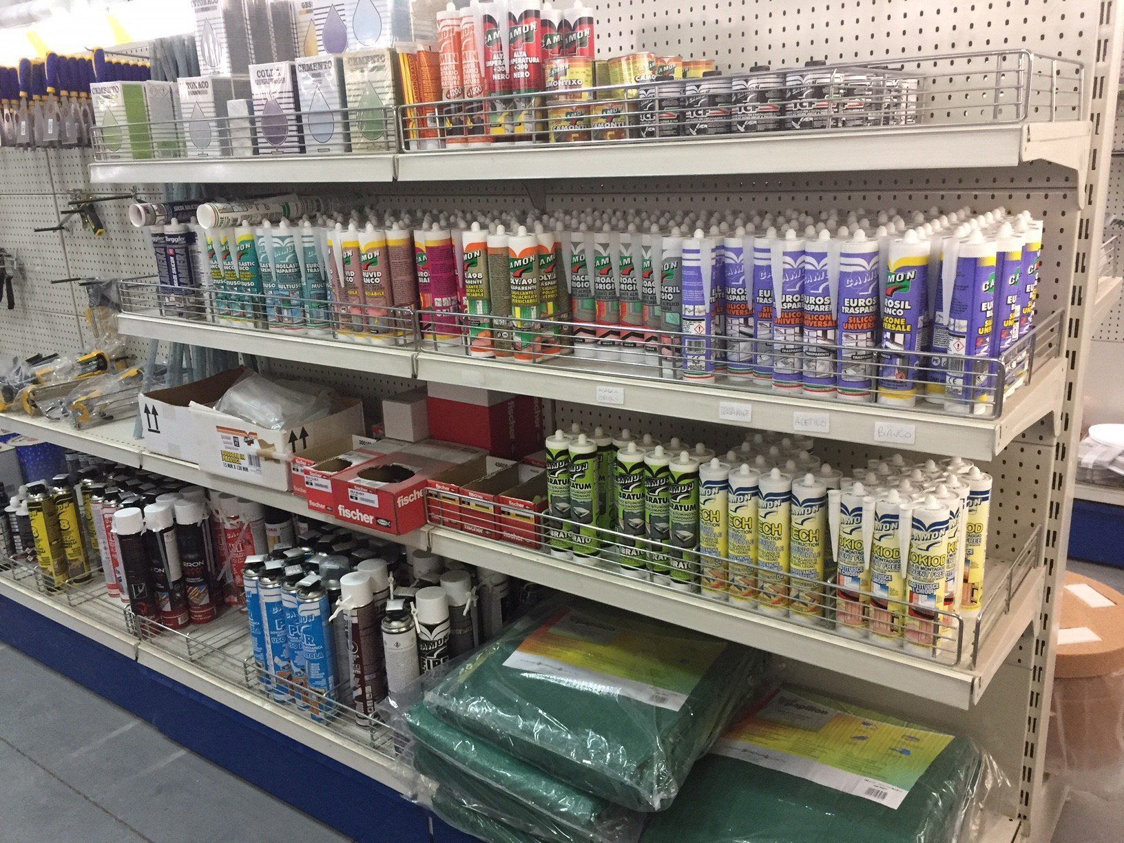 Scaffali di un negozio pieni di vari tubi e contenitori di sigillante e altri materiali edili.