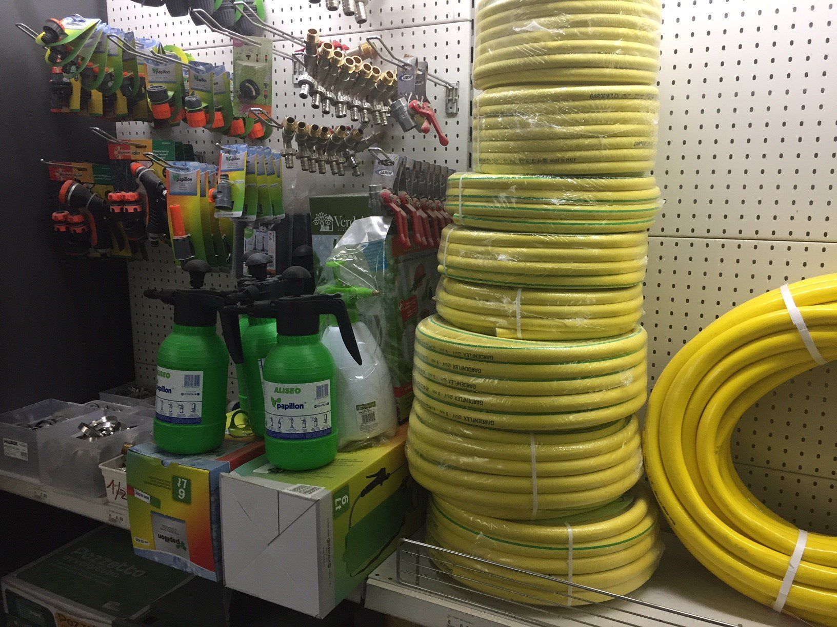 Espositore in un negozio, con tubi da giardino, flaconi spray e attrezzi. I tubi sono gialli.