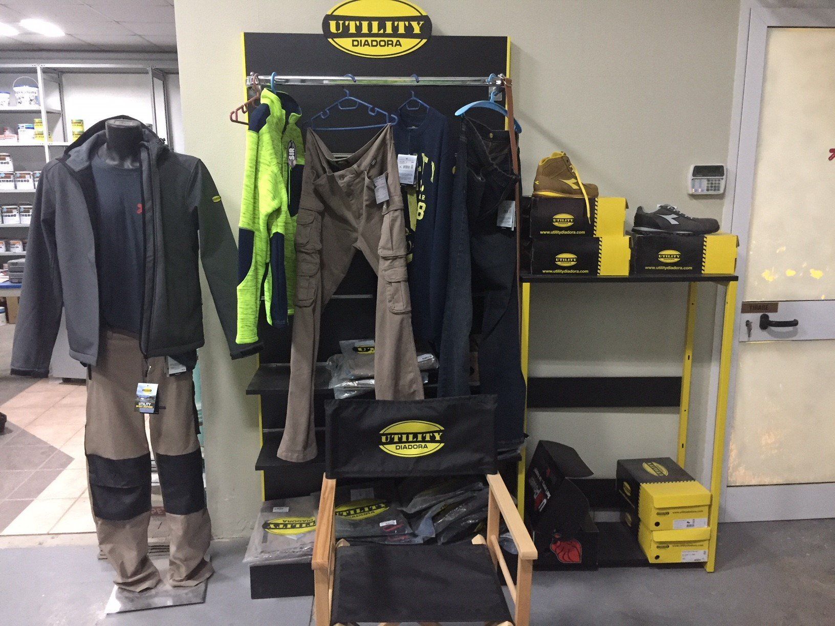 Esposizione di abiti da lavoro: giacca, pantaloni e calzature. Un manichino, un appendiabiti, una sedia e uno scaffale con scatole.