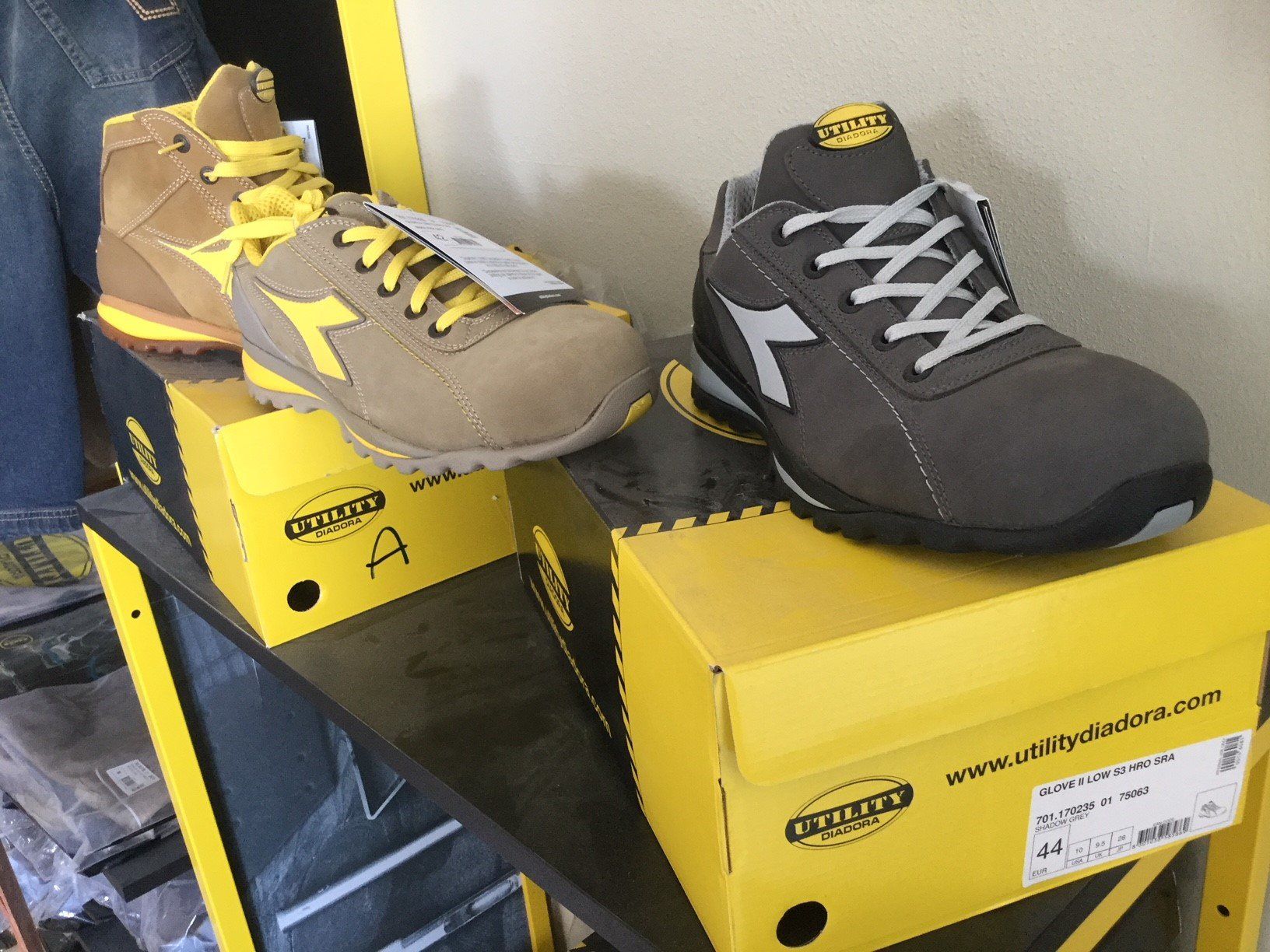 Scarpe antinfortunistiche di vari colori e stili esposte su scatole gialle.