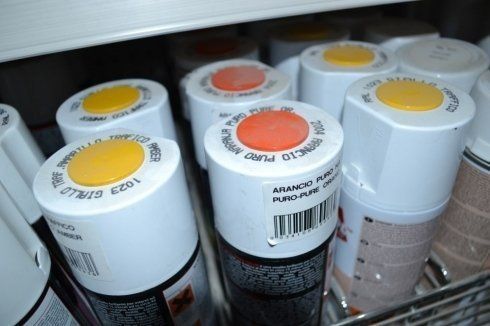 Primo piano di bombolette spray con tappi colorati, tra cui giallo e arancione, in un negozio.
