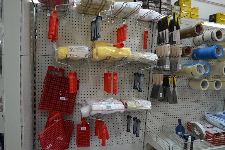 Forniture per la pittura esposte su una parete di un negozio, tra cui rulli, pennelli e nastro adesivo. Articoli rossi, gialli, bianchi e blu.