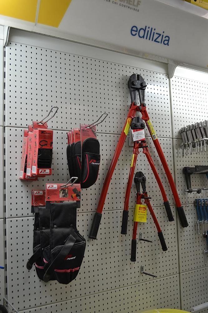 Tronchesi e guanti da lavoro appesi alla parete di un espositore per negozi.