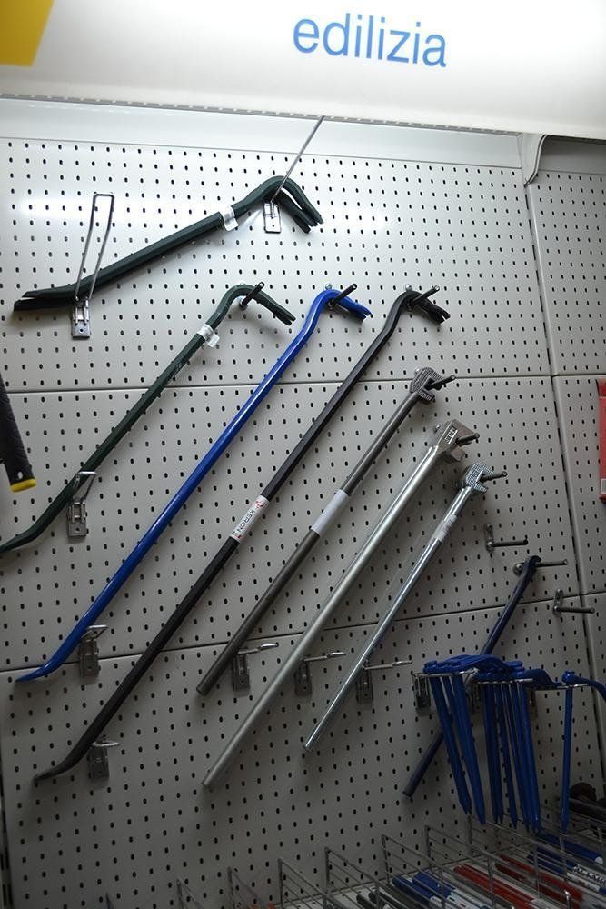 Piedi di porco di vari colori esposti su una parete forata in un negozio di ferramenta.