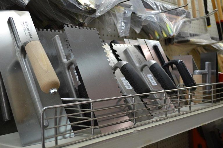 Fila di cazzuole sullo scaffale di un negozio, di varie dimensioni e con diversi tipi di impugnatura.