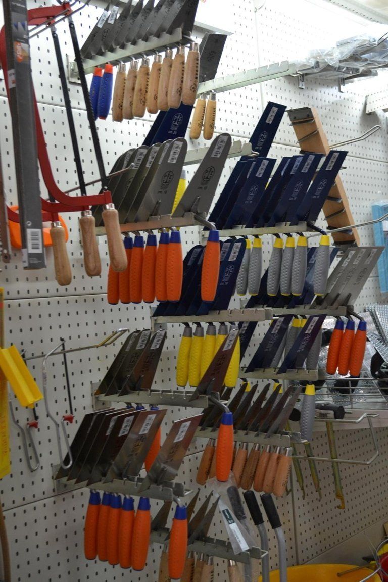 Assortimento di cazzuole e utensili esposti su un pannello forato in un negozio di ferramenta.