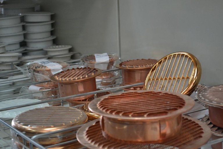 Oggetti metallici color rame, probabilmente utensili da cucina, impilati sugli scaffali di un negozio.