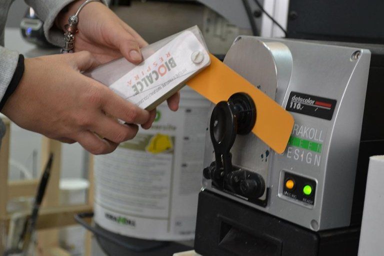 Una persona posiziona la scatola di un prodotto su un applicatore di etichette. La macchina è grigia con luci verdi e arancioni.