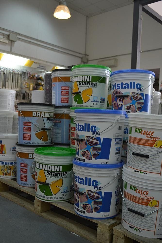 Barattoli di vernice impilati su pallet in un negozio. Etichette visibili, coperchi verdi e blu.